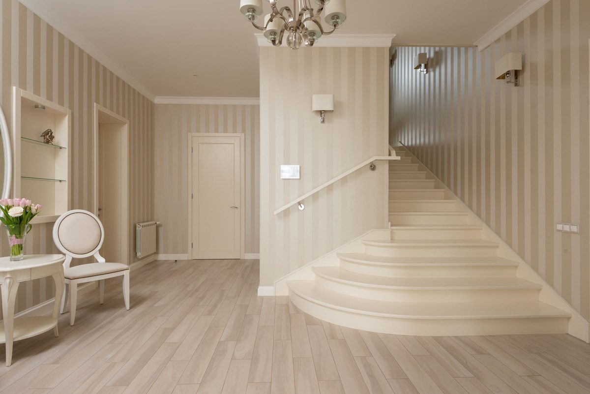 Elegant curved staircase finished with beige tone-on-tone striped wallpaper