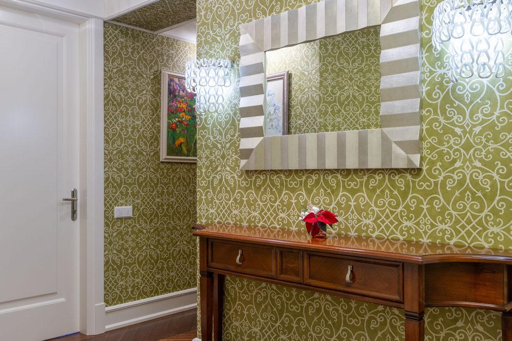 Hallway lined with olive-green damask scroll wallpaper, a wood console and a mirror