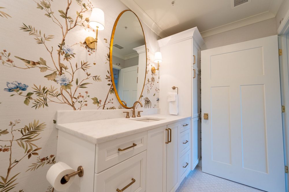 Powder room with chinoiserie botanical wallpaper framing a gold oval mirror