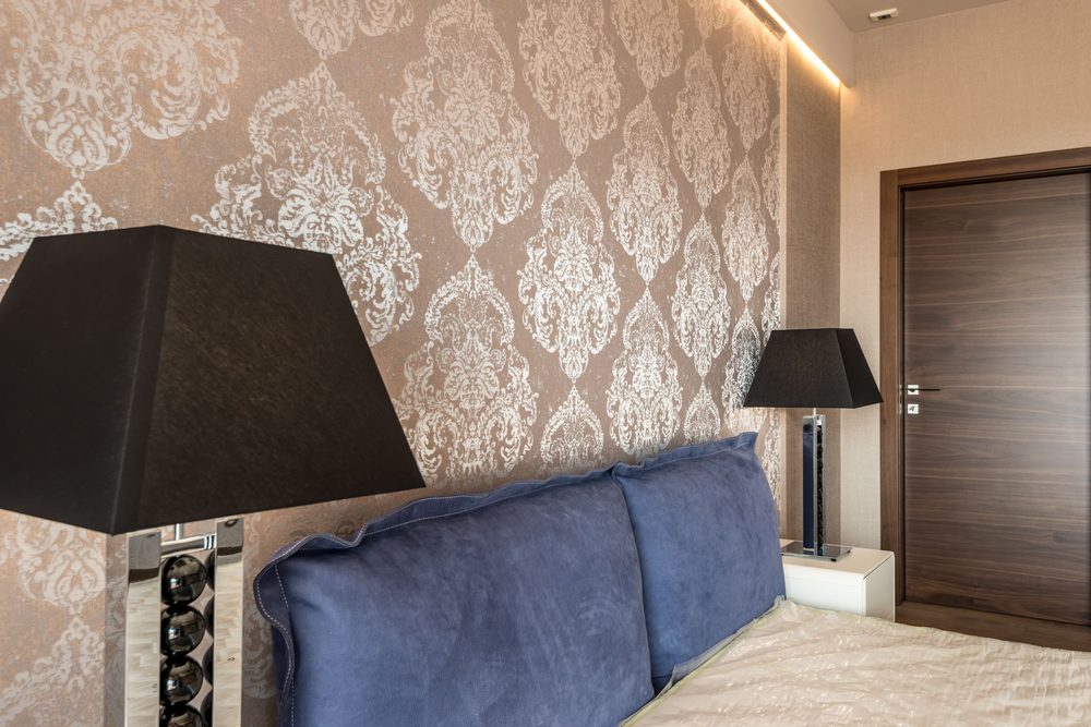 Bedroom with brown-and-silver damask accent wall behind a navy upholstered headboard
