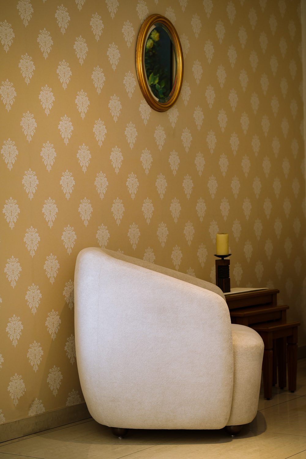Cozy corner with gold damask wallpaper, a cream bouclé armchair and a small gilt mirror