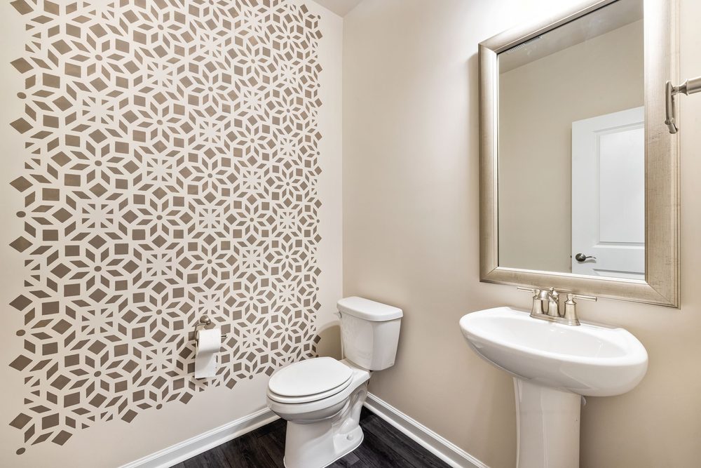 Powder room with a taupe geometric floral accent wall and clean trim edges around a pedestal sink
